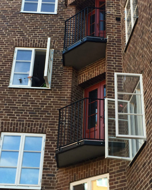 Svarta balkonger mot en brun tegelfasad. Vita fönster pryder också fasaden.